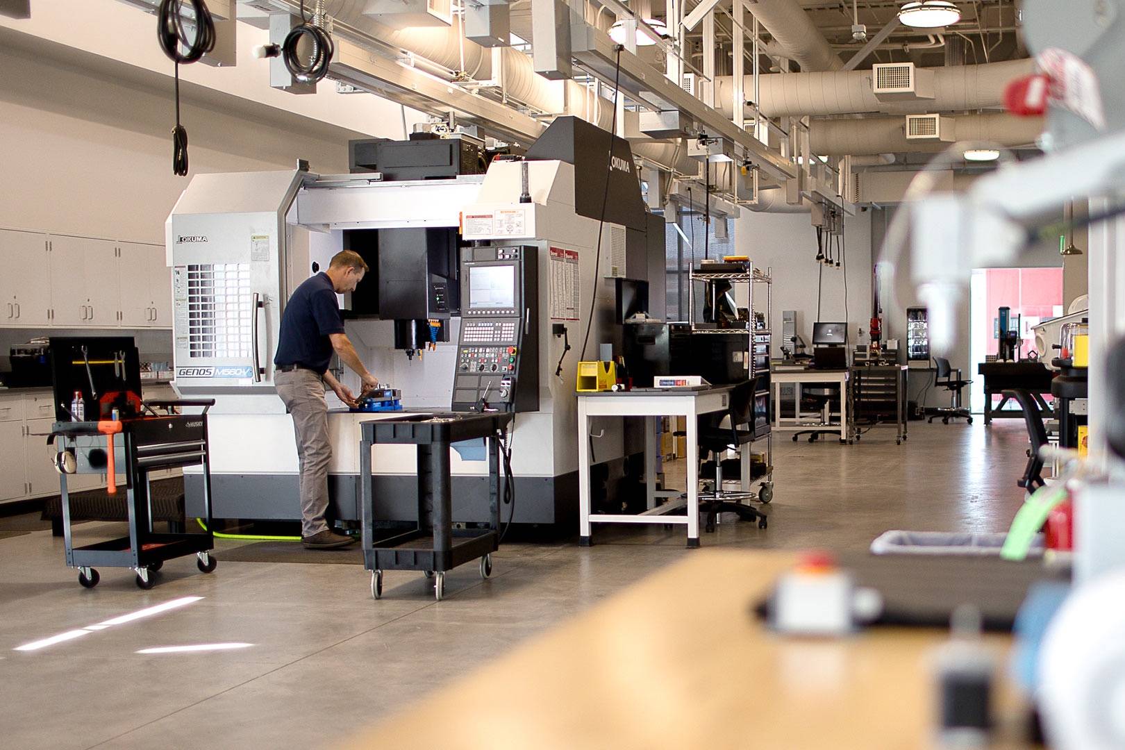 Setting up a part on a CNC machining center in an AES building lab, with workbenches and test stations behind.